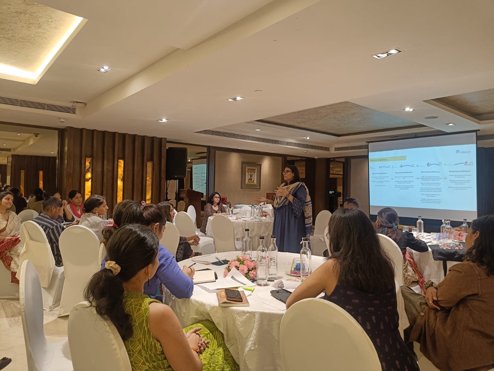 Groups of people sitting at tables listening to a speaker give a presentation